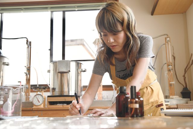 蒸留器の前で記録をつける娘